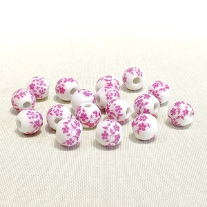 Detailed view of 10mm white ceramic beads with purple floral patterns on fabric