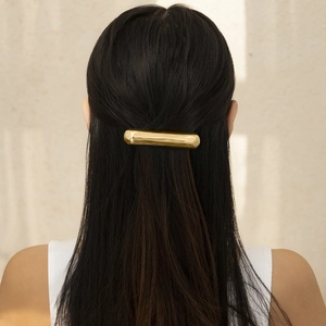 Detail of minimalist gold cylindrical metal hair tie on dark hair with glossy finish