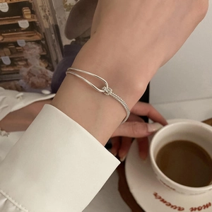 Elegant silver knotted chain bracelet styled with a white shirt and coffee cup background