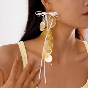 Detail of sweet bow earrings with yellow shell-like discs and white pearls on a model