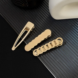 Close-up of three gold metal hair clips on glass tray including triangle and rectangle styles
