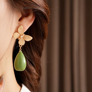 Détail de boucles d'oreilles papillon dorées vintage avec goutte en résine verte sur modèle