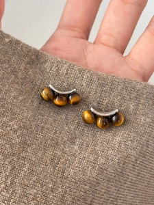 Detail view of silver curved earrings with three tiger eye stones on brown fabric