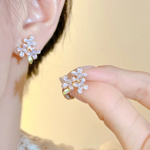 Close-up of lavender flower earrings with golden details worn on ear and held by hand