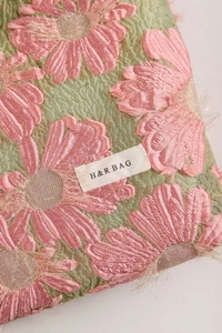Macro shot of pink floral jacquard fabric with fringe details and woven logo label