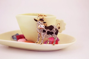 Cute cow keychain with clear rhinestones and black enamel set on a white teacup