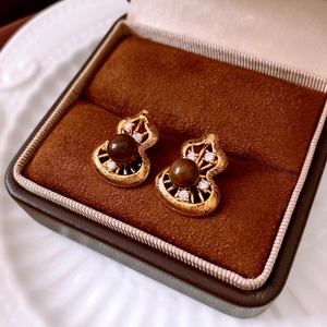 Macro view of gold gourd earrings with brown beads and small diamonds in a velvet box