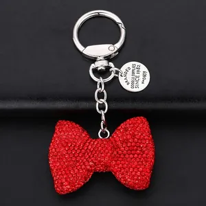 Close-up of red rhinestone bow keychain with vintage metal tag on black leather background