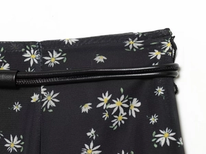 Dettaglio del tessuto floreale nero con margherite bianche e cintura sottile in pelle