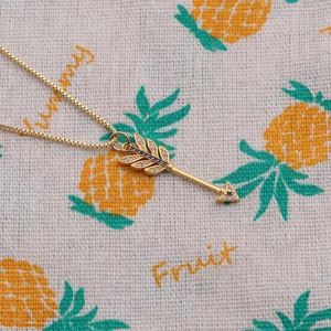Gold-plated arrow pendant necklace with blue and white zircons on a fabric backdrop
