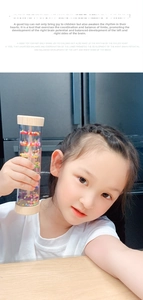 Detail of a child holding a wooden rainmaker tube toy showing colorful beads inside