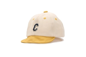 Close-up of baby baseball cap featuring beige fabric with yellow brim and navy letter C patch