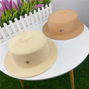 Close-up of woven straw boater hats with round gold M logo charms in beige and tan