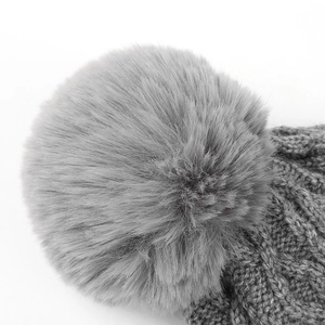 Dettaglio di un cappello grigio a maglia con pompon in ecopelliccia e trama a trecce