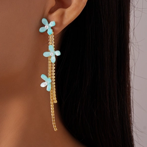 Detail of blue resin flower earrings with dangling gold rhinestone tassels worn by a model