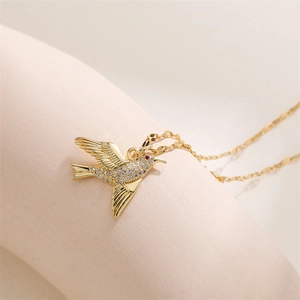 Détail du collier pendentif oiseau doré avec cristaux blancs et œil en gemme rouge