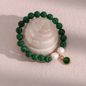 Detail of malachite beaded bracelet with pearls and gold emerald pendant on a shell