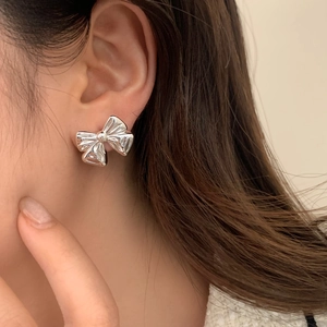 Elegant silver bow earrings with polished ribbon design on a model's ear in minimalist style