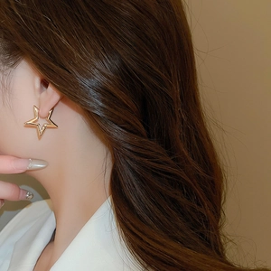 Detailed close-up of a model wearing a gold hollow star earring with a polished metal finish