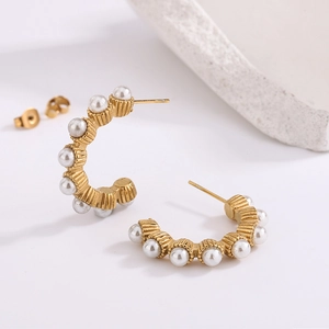 Detail of C-shaped gold earrings featuring vertical texture and multiple white pearls