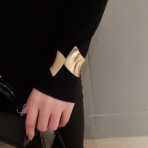 Dettaglio di un bracciale rigido dorato irregolare indossato su una manica nera