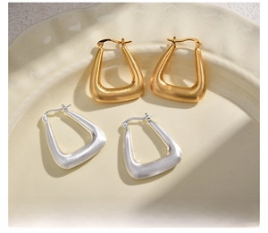 Detailed macro view of gold and silver brushed metal trapezoid hoop earrings on a ceramic dish