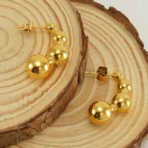Macro shot of 18k gold plated pea-shaped stud earrings on natural wood grain background
