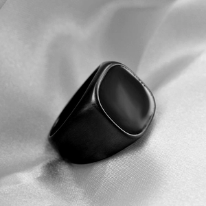 Macro shot of matte black square signet ring with brushed metal texture on grey silk