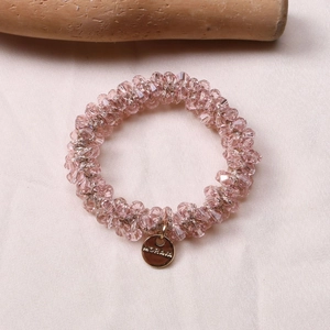 Detailed macro of pink crystal beads and a gold metal brand pendant on the elastic hair tie