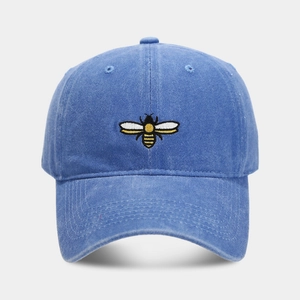 Close-up of detailed yellow and black bee embroidery on a washed blue cotton baseball cap