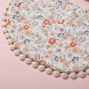 Détail du bavoir floral pour bébé avec bordure pompon sur fond rose doux