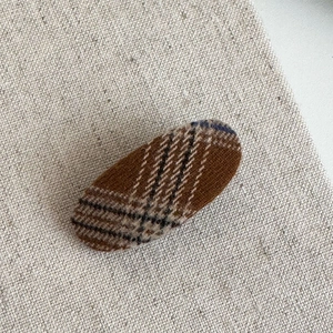 Detailed view of an oval brown plaid hair clip with classic British check wool fabric