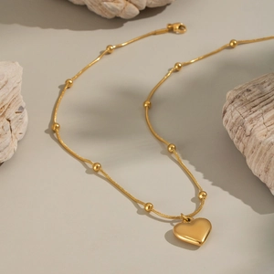 Collier avec pendentif cœur doré et chaîne à billes sur pierres naturelles avec lumière douce