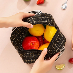 Insulated black tweed lunch bag with striped handles filled with fresh colorful fruits