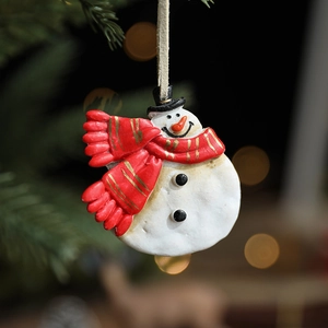 Resin snowman Christmas ornament with red scarf and black hat on festive pine background
