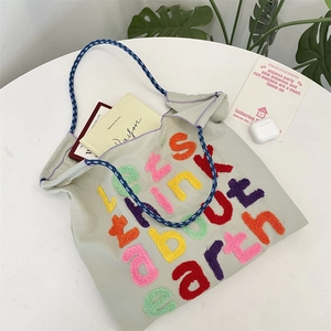 Detail of canvas tote with colorful embroidery and woven handles on a white table