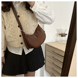 Brown semi-circular leather crossbody bag shown in a lifestyle scene with a warm aesthetic