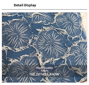 Close-up of vintage blue denim fabric featuring white floral fringe and raw edge details