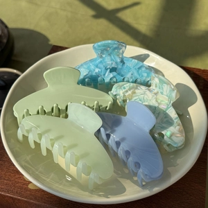 Close-up of five colorful acetate hair claws in a white tray with natural lighting