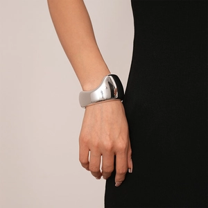 Close-up of sculptural irregular silver metal cuff bracelet on model wearing black dress