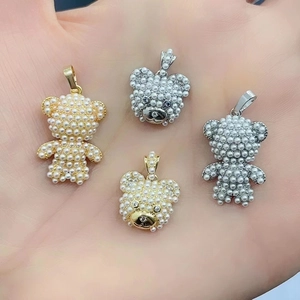 Macro detail of gold and silver bear pendants with inlaid pearls held in hand