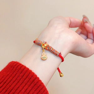 Détail d'un bracelet tressé rouge porte-bonheur avec breloque en émail au poignet