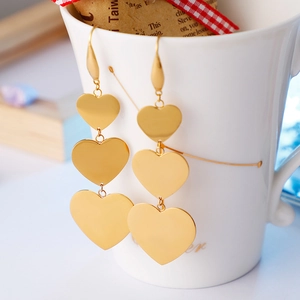 Three-tier gold heart drop earrings hanging on a white ceramic cup edge
