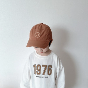 Détail d'une casquette marron enfant avec broderie smiley et t-shirt blanc 1976