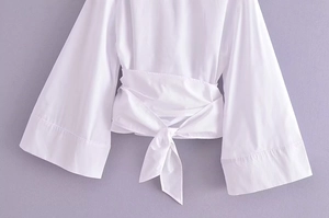 Détail du chemisier cache-cœur blanc avec manches cloche et nœud de serrage à la taille