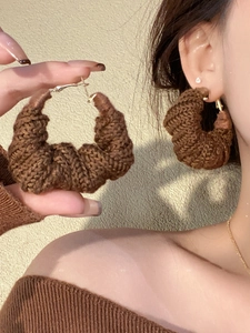 Macro shot of dark brown knitted croissant hoop earrings with gold metal clasp on model