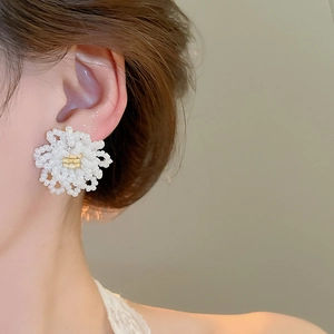 Macro detail of white beaded flower earrings with gold center worn on earlobe