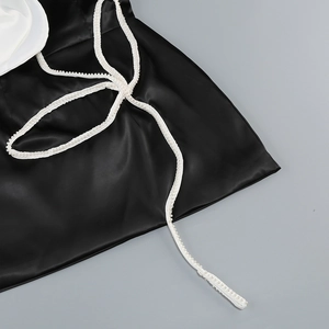 Détail d'une robe en satin noir avec bretelles en perles blanches et laçage croisé