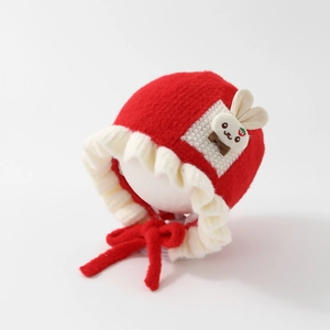Close-up of a cute red baby knit hat with rabbit decor and soft white ruffle edge