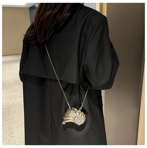 Detailsicht der silbernen Metallic-Schnecken-Clutch am Model im schwarzen Mantel